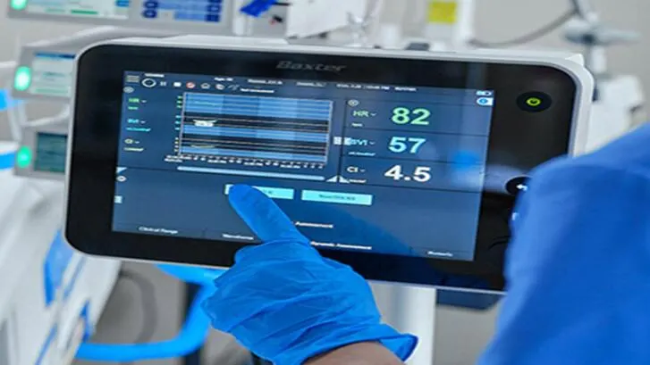 A healthcare worker in medical gloves pressing buttons on the screen of a baxter device