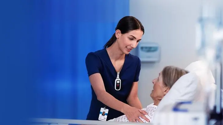 A healthcare worker with a tracking device comforts a patient in a hospital bed