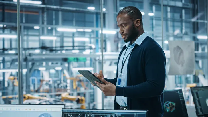 A man in the office of a manufacturing plant writing on a tablet