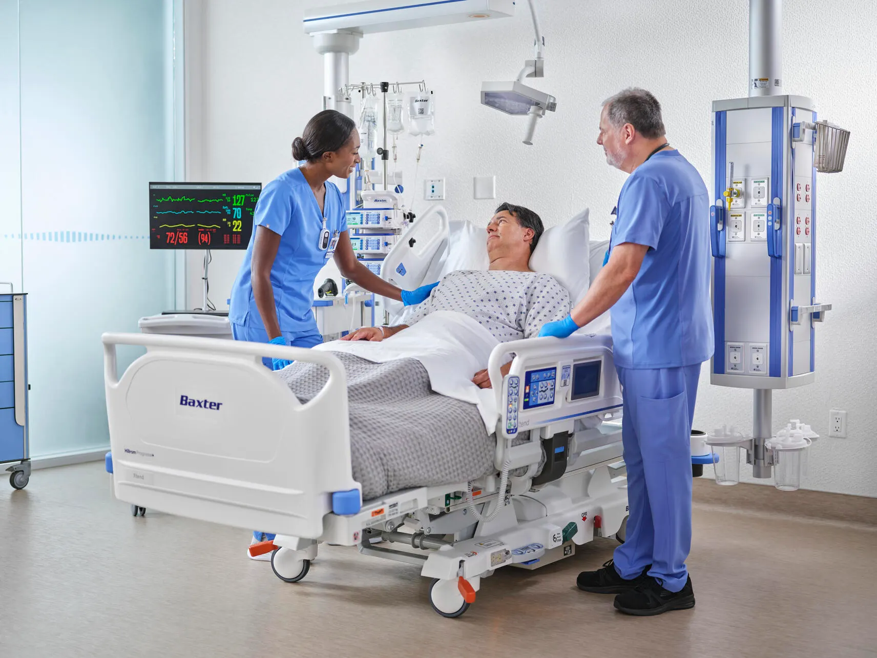 Two healthcare workers talk to a patient in a hospital bed