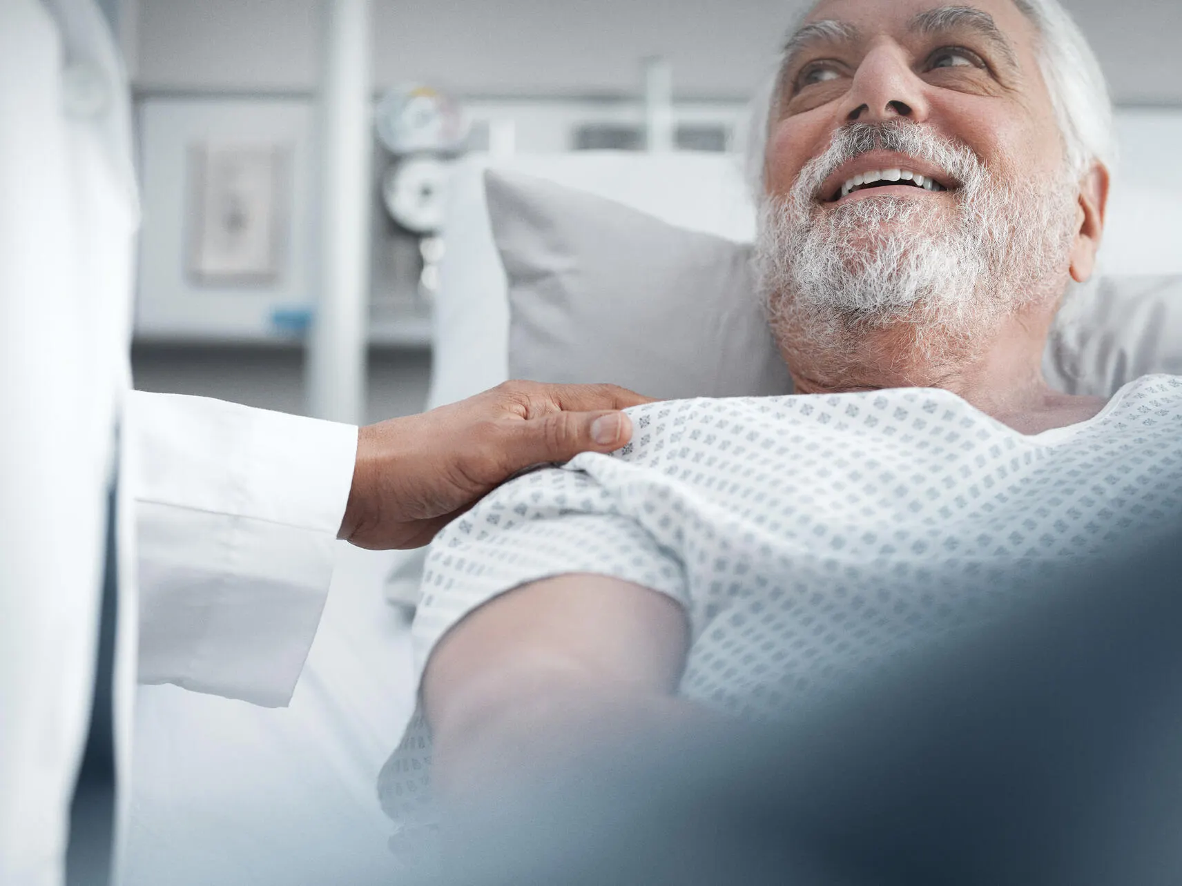 Patient in a hospital bed smiles at a healthcare worker touching their shoulder