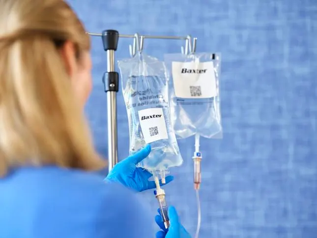 The back of a physician as she adjusts a Baxter IV bag