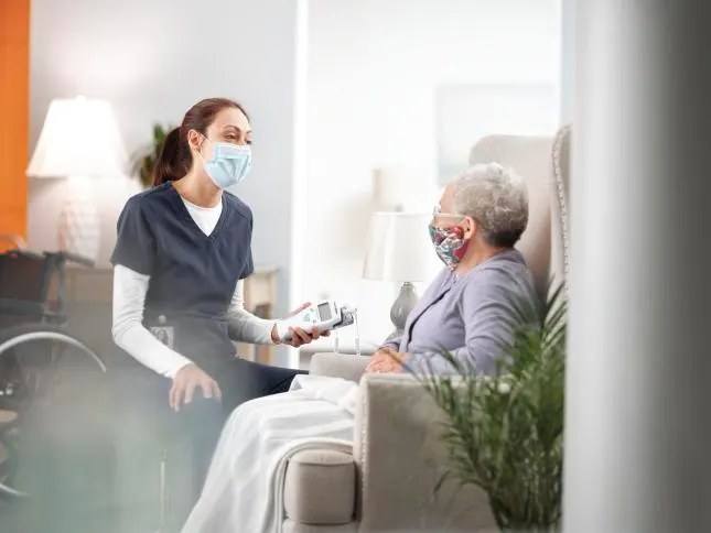 Long term care worker holds a SureTemp Plus near a sick patient