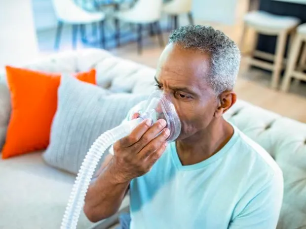 Older man sitting on couch using Synclara Cough System