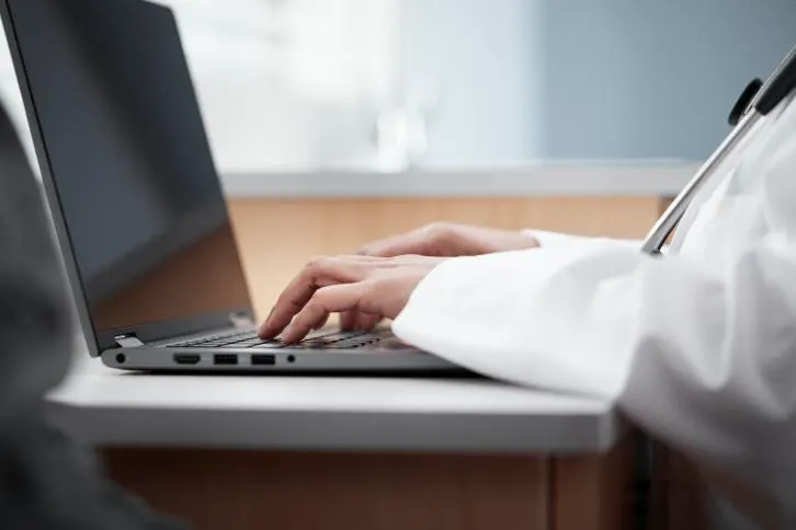 Hands wearing a lab coat type on a laptop