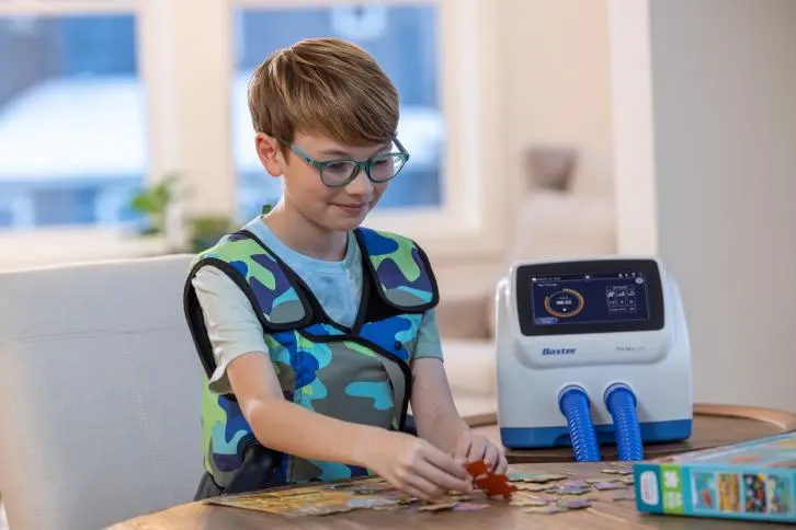 Child wearing a respiratory vest assembles a jigsaw puzzle.