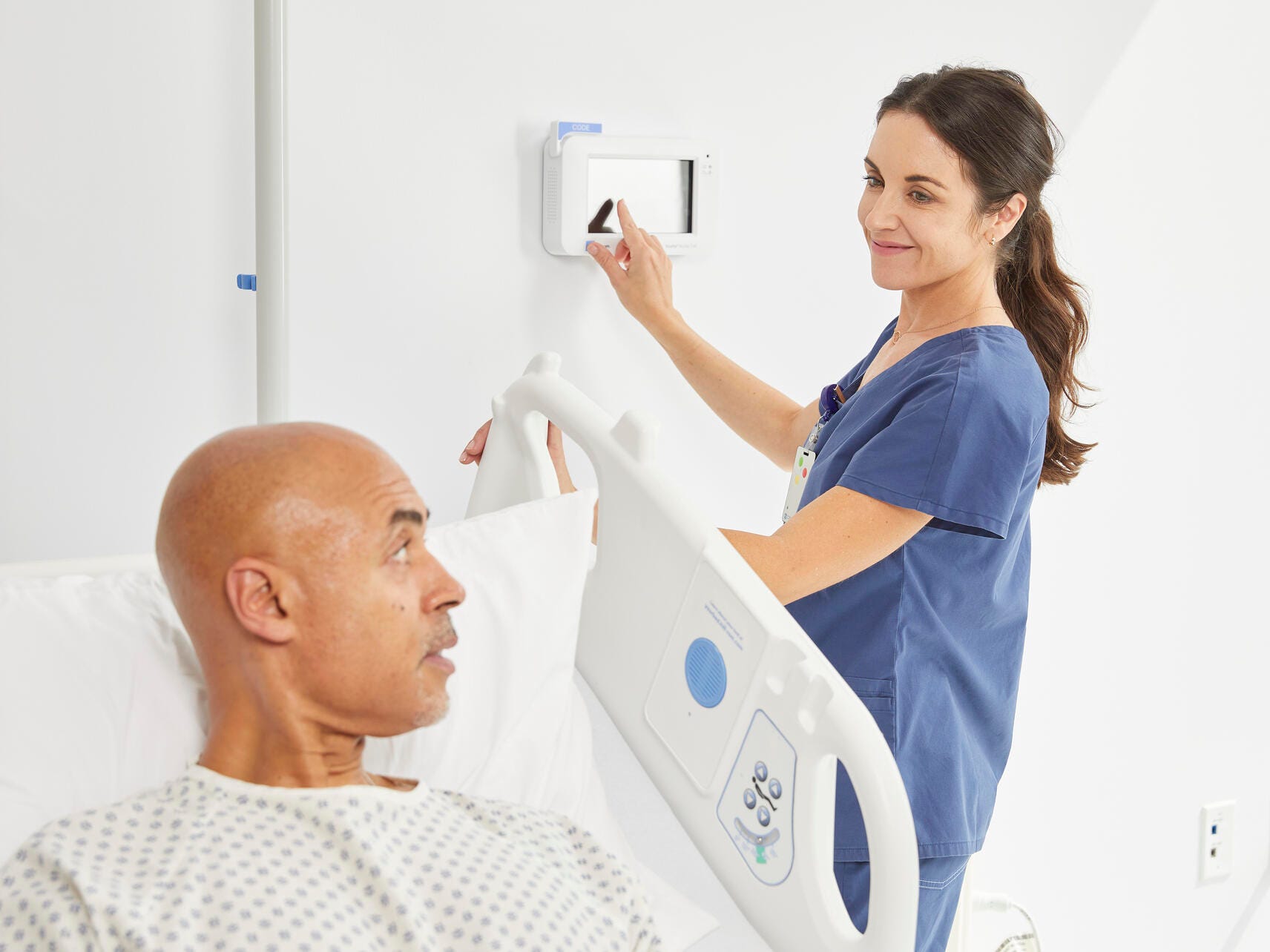 Nurse adjusts a wall communication unit next to a patient in a hospital bed