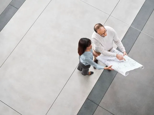 Two professionals review architectural drawings in an open indoor space
