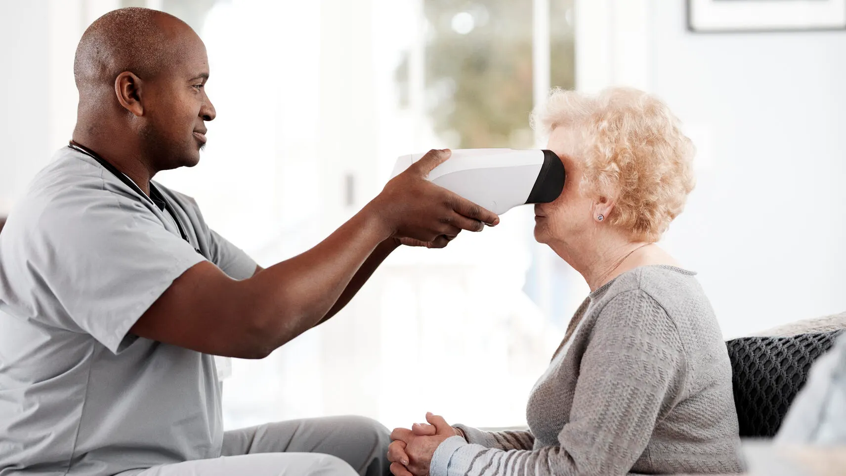 A healthcare professional holds the RetinaVue 700 to a patient's face in a home setting