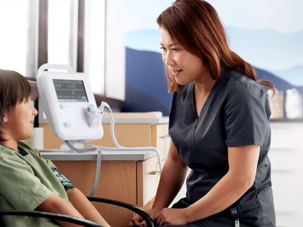 A boy sitting in chair with nurse and vital signs monitor