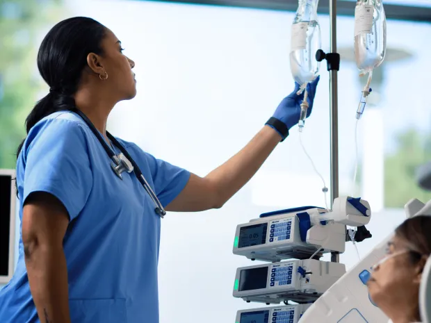 Healthcare worker adjusts an IV bag attached to an infusion pump