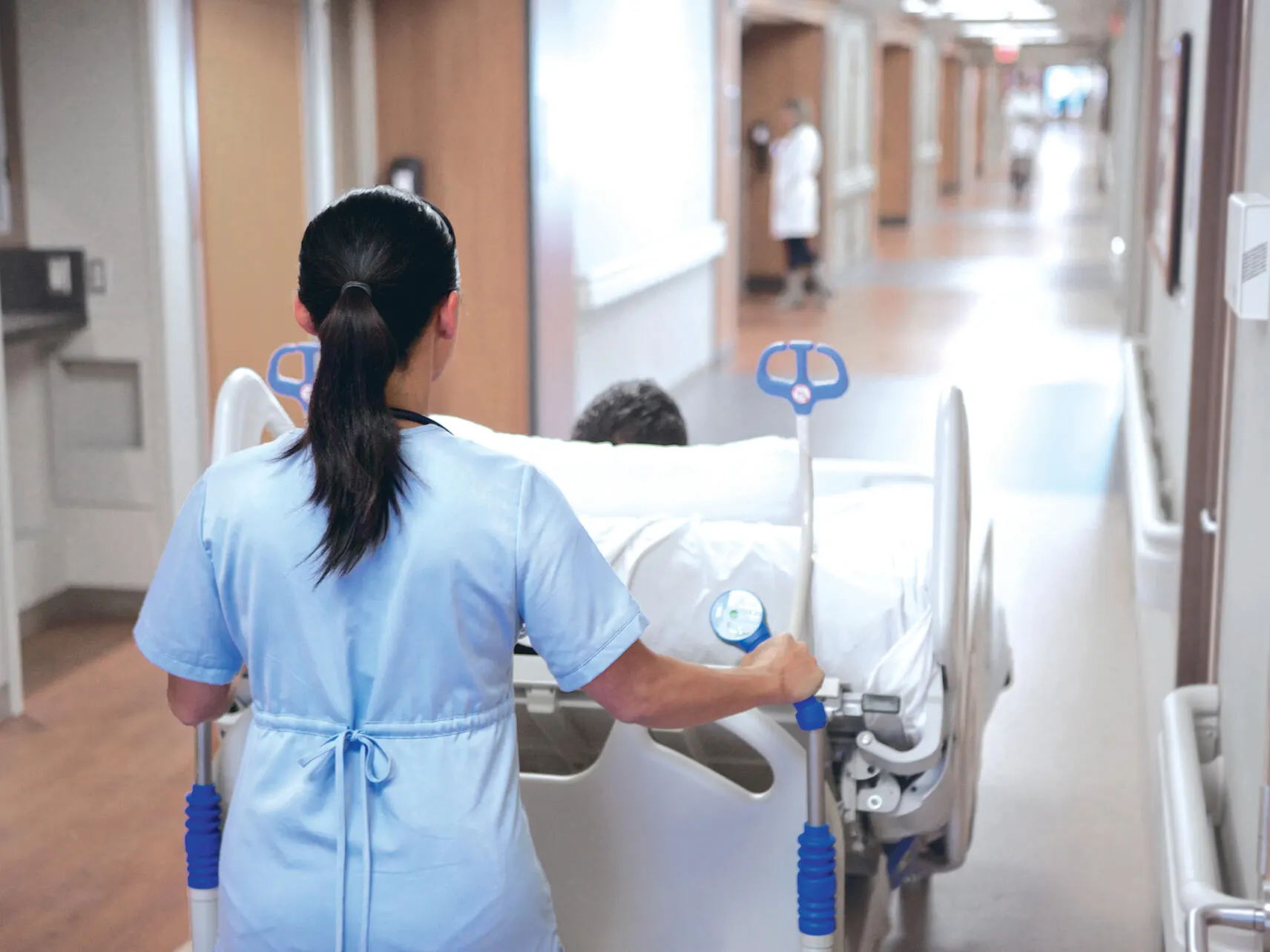 A nurse wheeling a Compella bariatric bed down a corridor