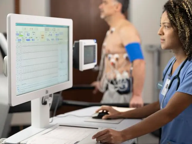Healthcare professional looking at ECG data while a patient walks on a treadmill while wearing electrodes
