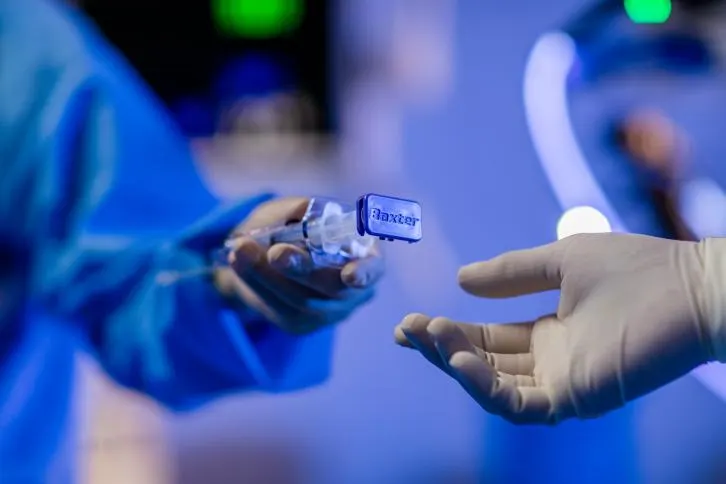 Surgeon passing a Baxter surgical tool to another surgeon