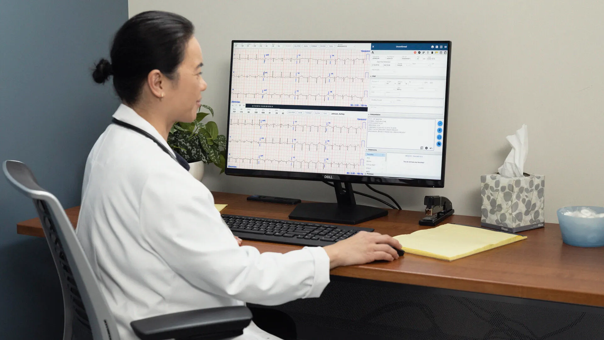 Physician makes patient notes next to an ECG readout on a computer monitor