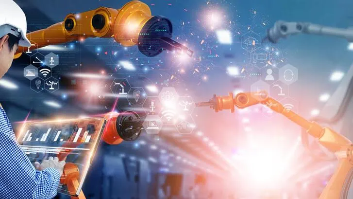 A worker in a hardhat manipulates a graphic with charts in front of robot manufacturing arms