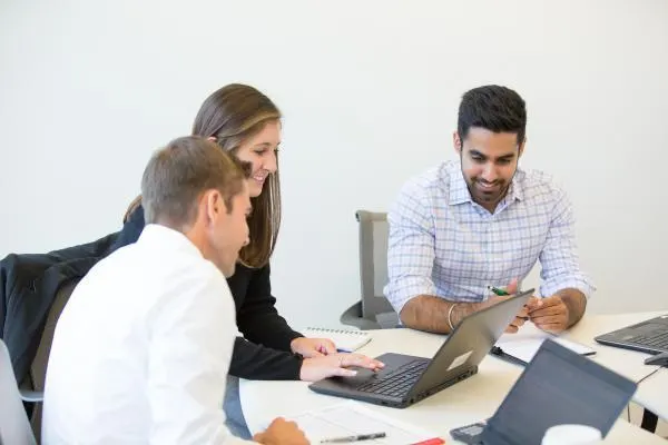 A group of people in office attire working together on a laptop at a desk