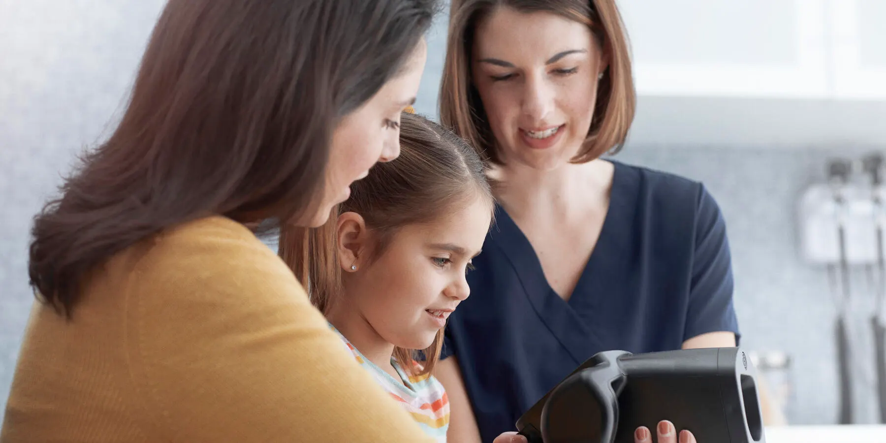 A healthcare worker shows the Spot vision screener to a parent and child