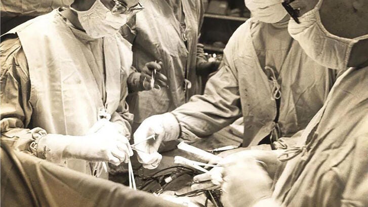 Surgeons work beneath a large, domed surgical light