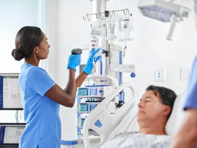 A healthcare worker scans the QR code on an IV bag next to a patient sleeping in a hospital bed