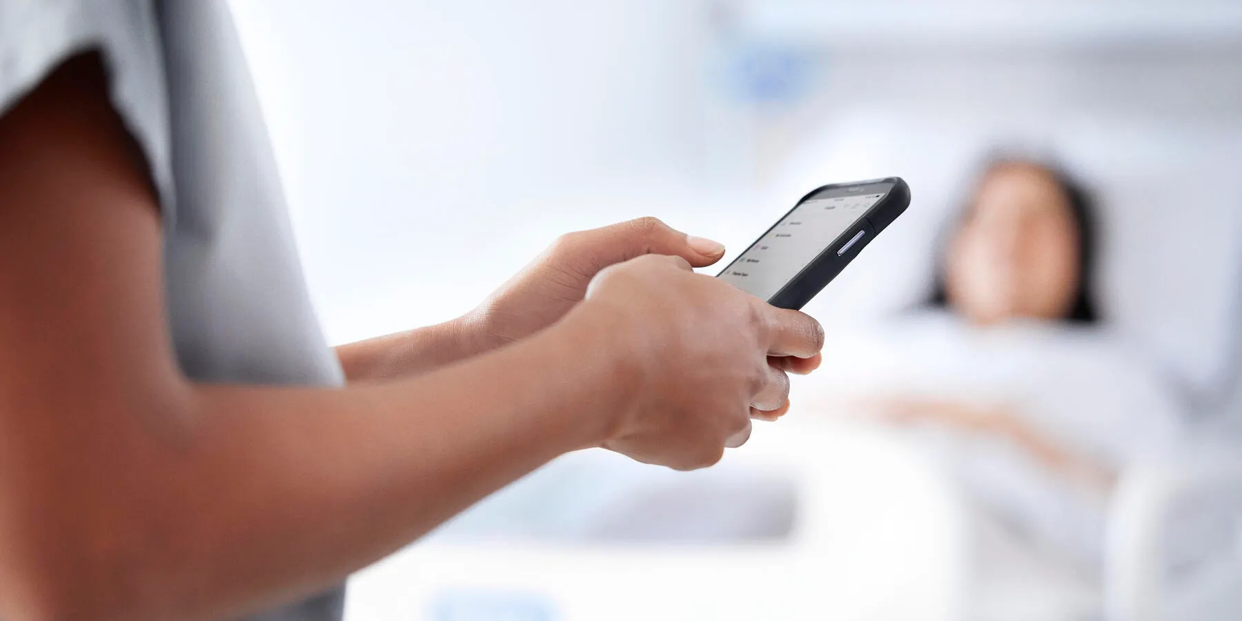 Healthcare professional enters data into a mobile phone next to a sleeping patient