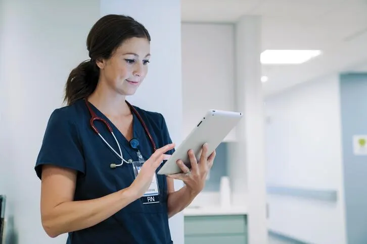 A healthcare worker types on a tablet in a hospital corridor