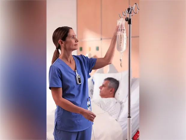 A healthcare worker wearing a Voalte Linq device adjusting an IV drip