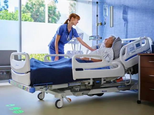 A healthcare worker touches the shoulder of a patient in a hospital bed