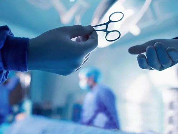 Gloved hands passing surgical forceps in an operating room
