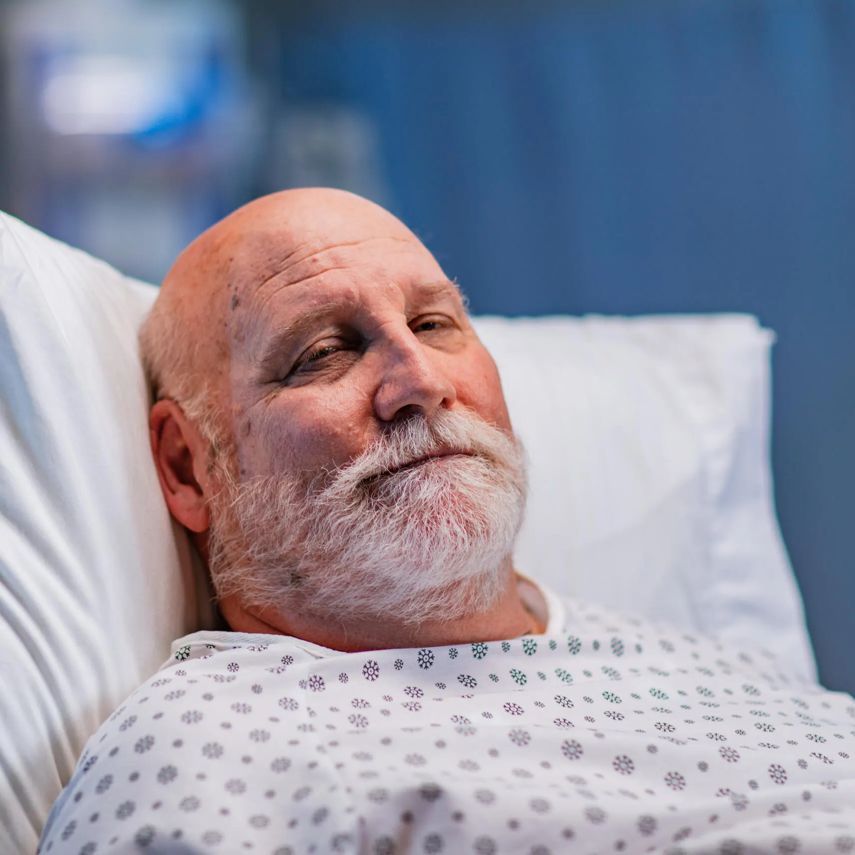 Patient in a hospital robe and hospital bed wearily smiling at the camera