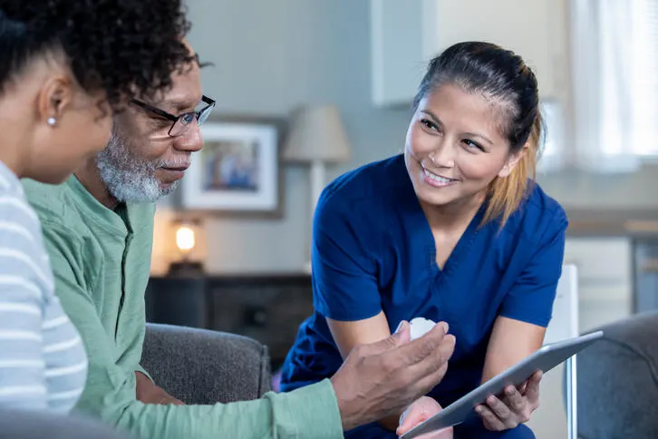 A clinician discusses the contents of a tablet with a man and a woman in a home setting.
