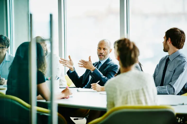 People in officewear have a conversation in a meeting room