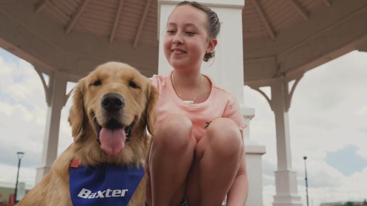 Izzy sits on a deck next to Baxter the dog, who is wearing a Baxter neckscarf