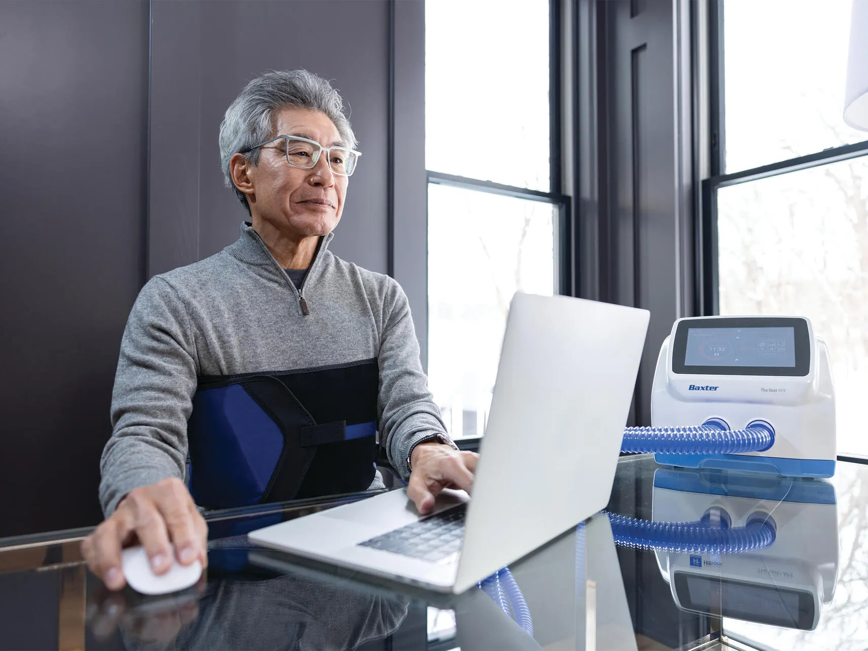 Elderly man wearing a Vest APX wrap garment works on a laptop at home