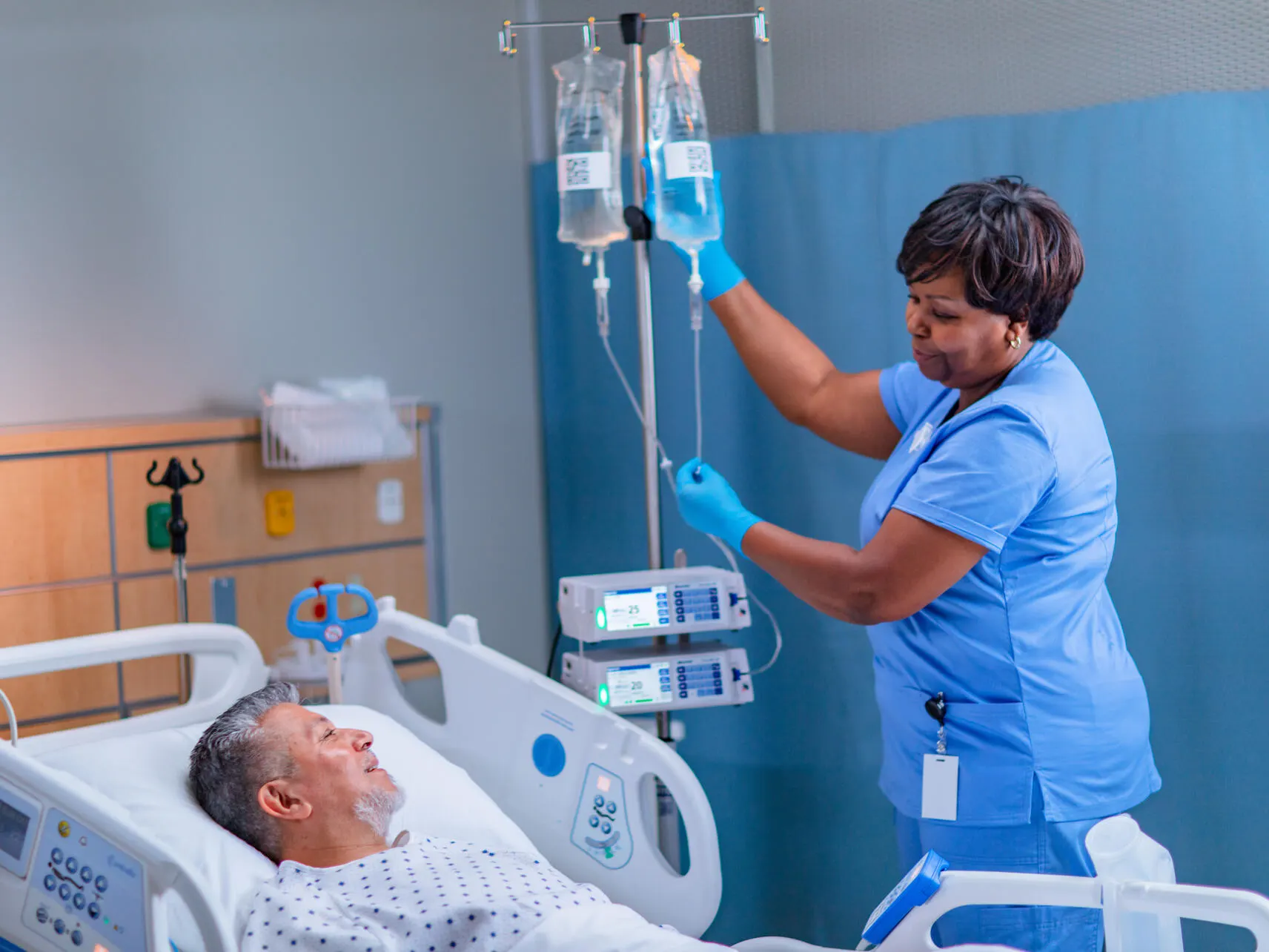 Nurse adjusts an IV drip next to a patient in a hospital bed