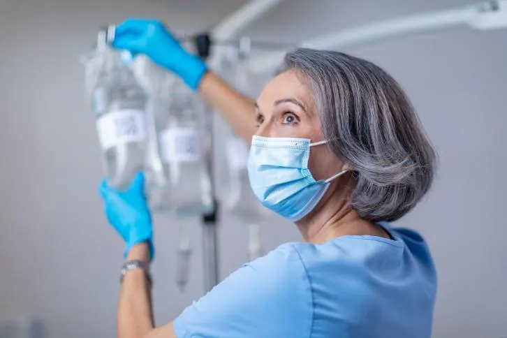 A clinician wearing gloves and a mask hanging up a IV bag while looking behind her