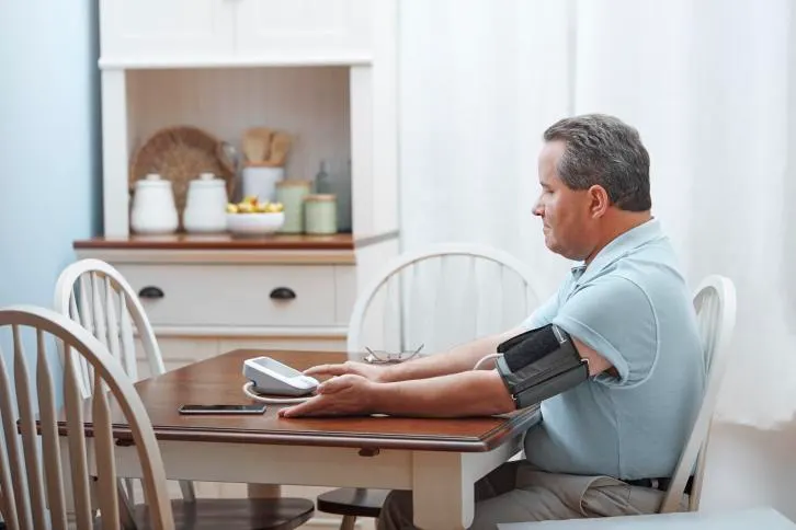 A man sits at his kitchen table and uses a Welch Allyn Home Blood Pressure Monitor.