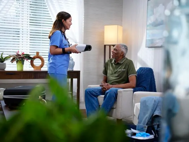 In a home setting, a healthcare worker holds the RetinaVue 700 while standing in front of an elderly man sitting in a chair.