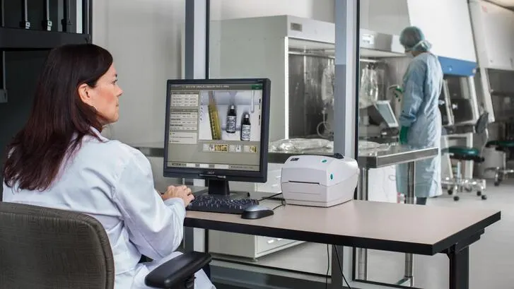 Laboratory technician examines images of vials on a computer monitor