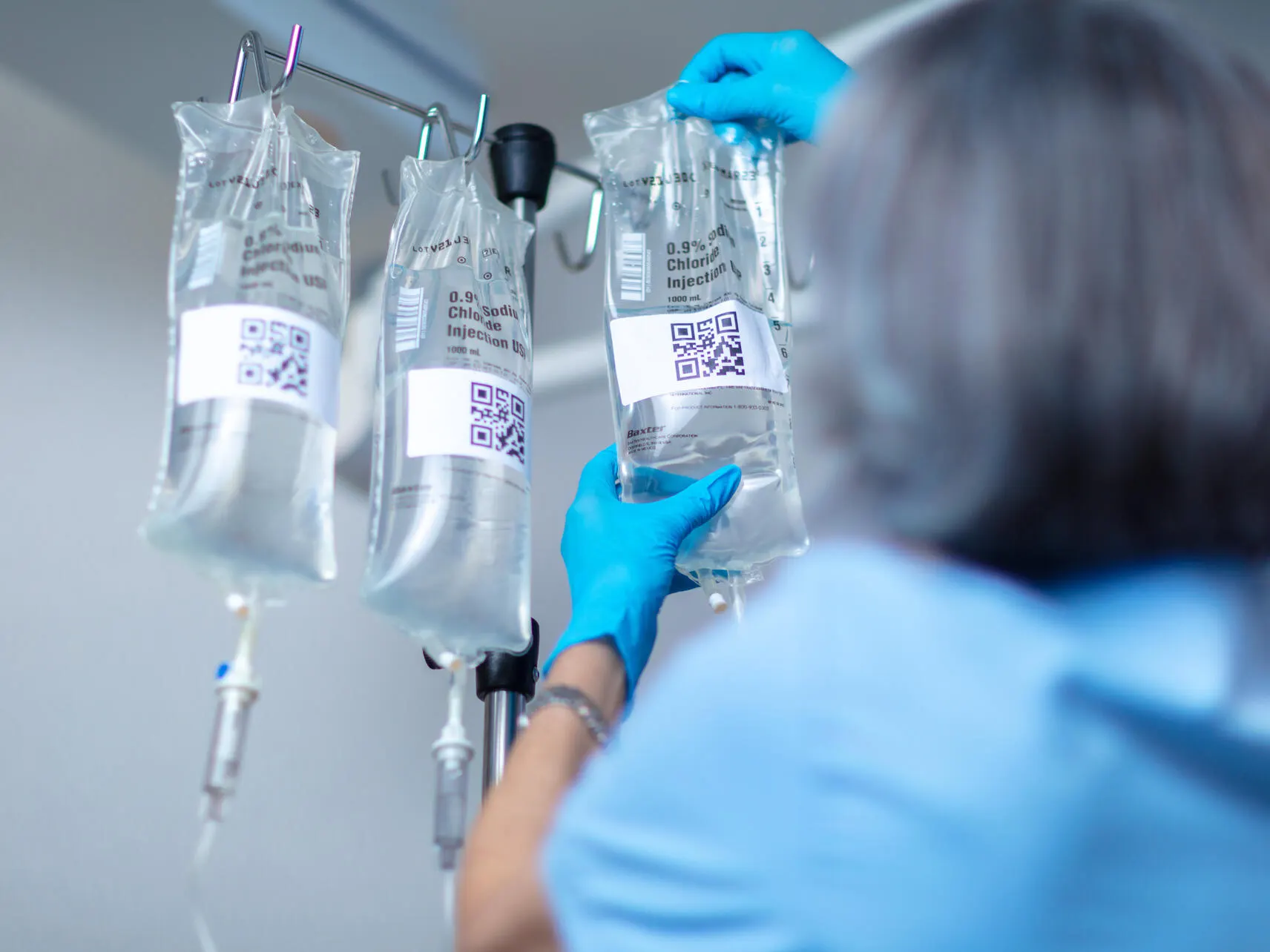 A healthcare worker hangs IV bags on an IV pole