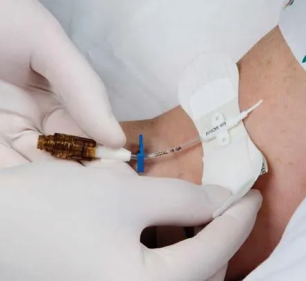 Hands in surgical gloves insert an IV needle in a patient's arm