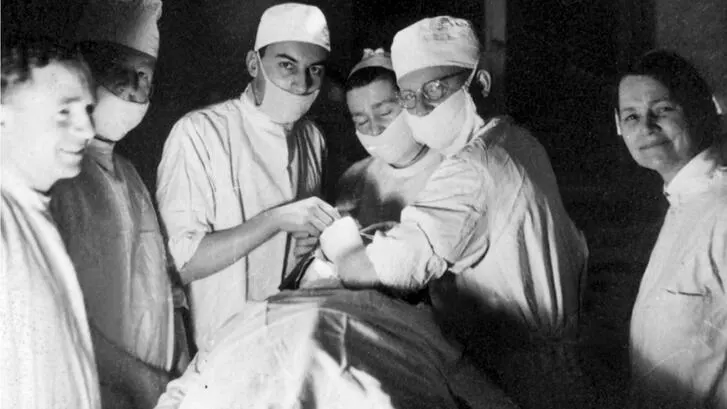 A mid-century surgical team works beneath a domed surgical light.
