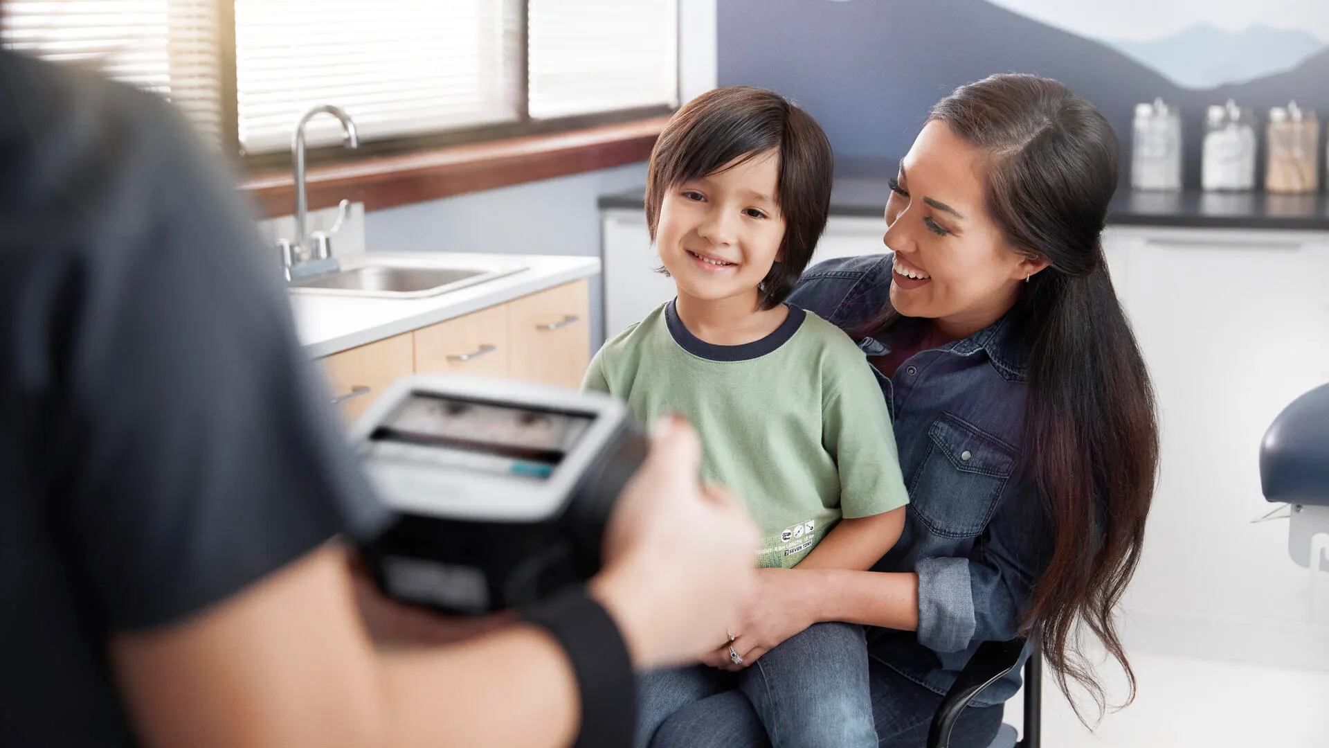 Mother and child smiling at each other in front of a clinician using the Spot vision screener