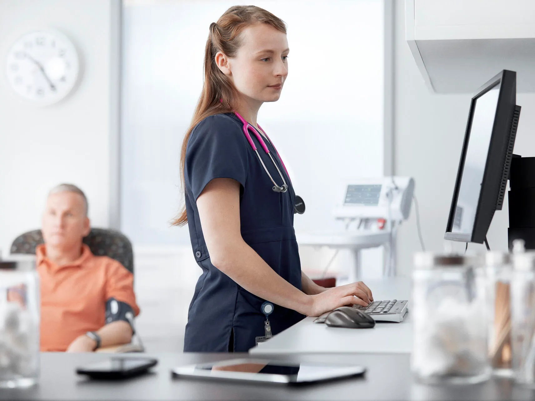 Healthcare professional working on a computer near a patient having their vitals monitored