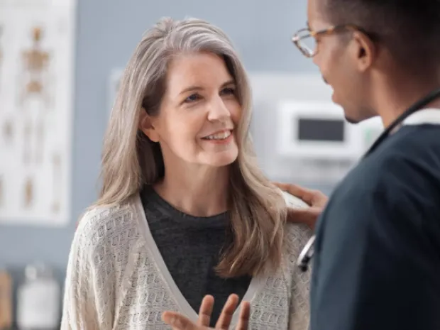 A clinician places his hand on a patient’s shoulder while talking in a primary care office.