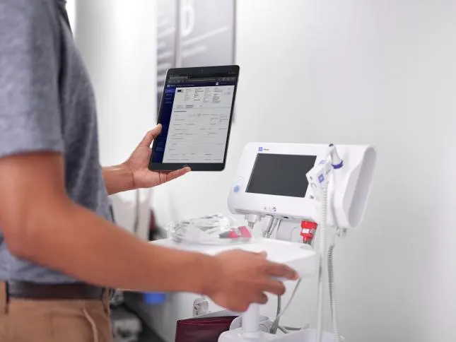 Biomed technician reads information off a tablet while repairing a device