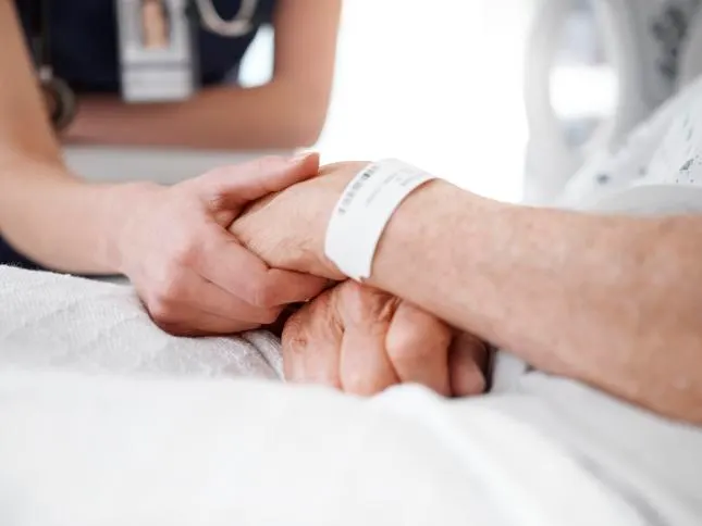 Healthcare professional holds the hand of a patient in a hospital bed with a medical wristband