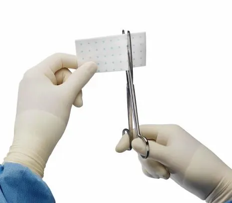 Hands in surgical gloves snipping a surgical patch with scissors