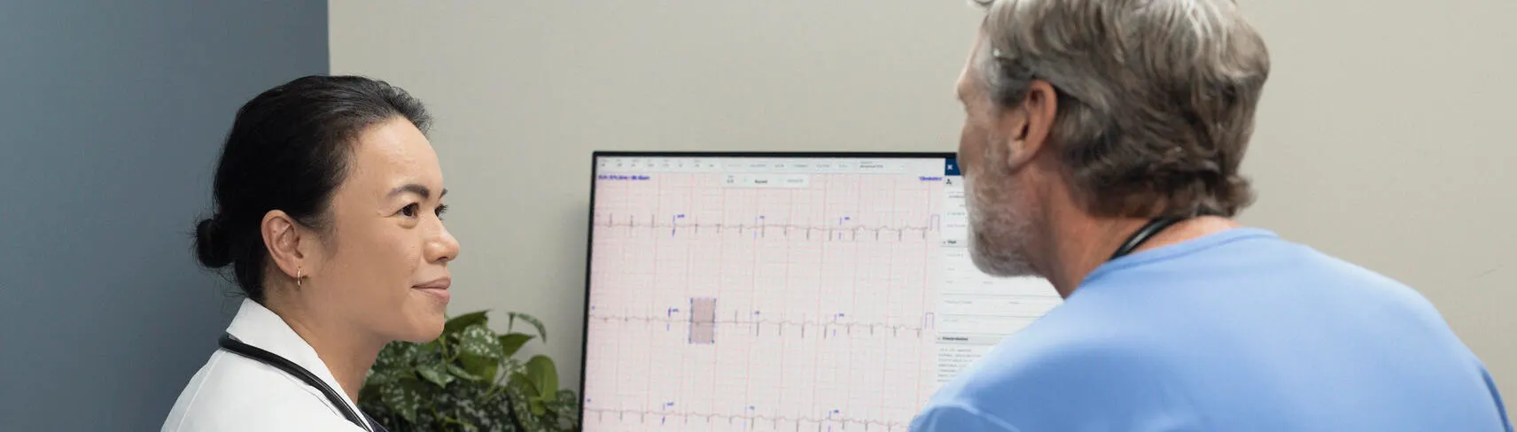 Doctor sitting down with physician looking at ecg report on computer screen
