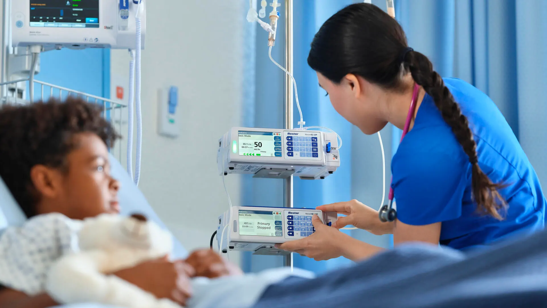 Pediatric patient with tedybear observing how a healthcare profesional adjusts the setitings of a  Clinolipid bag syringe pump